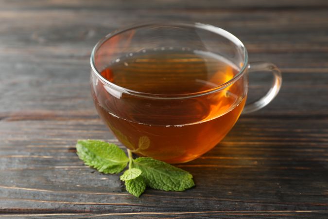 Cup of tea with mint on wooden background, close up