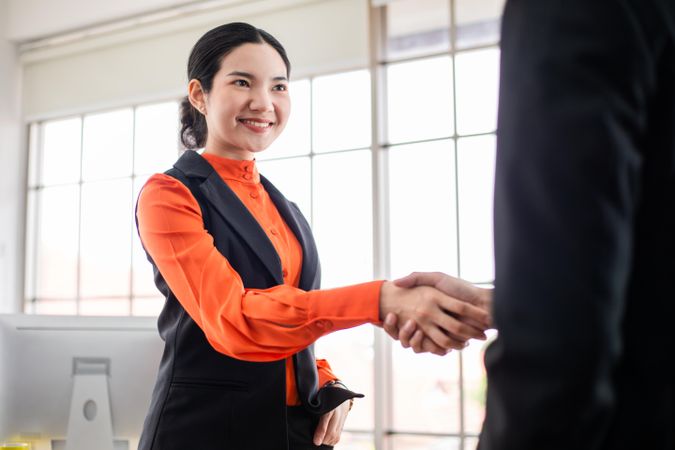 Woman in orange blouse reaching out to shake someone’s hand