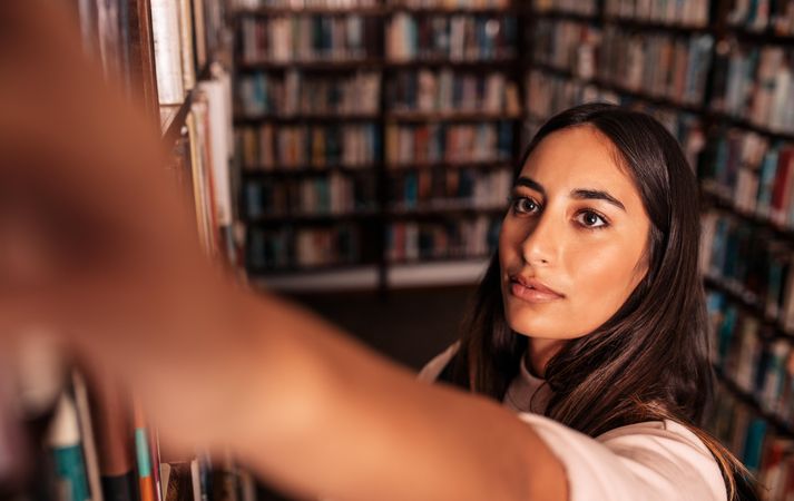 Female university student reaching for book in library