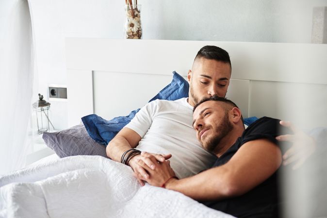 Smiling gay couple hugging and kissing on bed