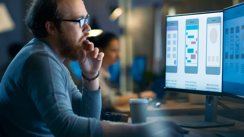 Male Mobile Application Developer Works with Graphics on His Personal Computer with Two Monitors.