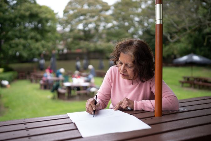 Older woman drawing in book on park bench