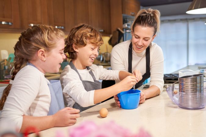 Laughing children cooking batter with mother in kitchen