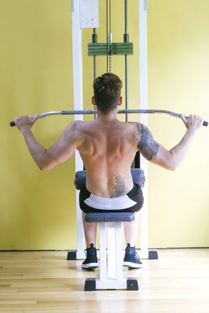 Back of tattooed male exercising his arms on pull down machine