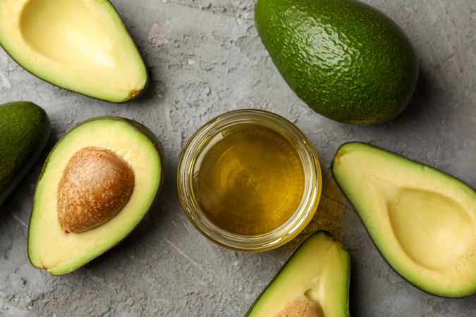 Ripe fresh avocado and oil on gray background, top view