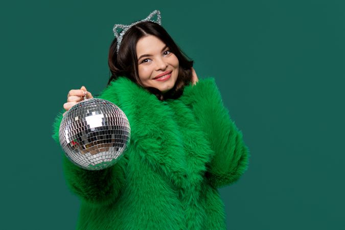 Smiling woman in green fur coat holding disco ball.