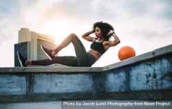 Side view of a female athlete doing abdomen crunches on rooftop fence of a building 5raMZ0