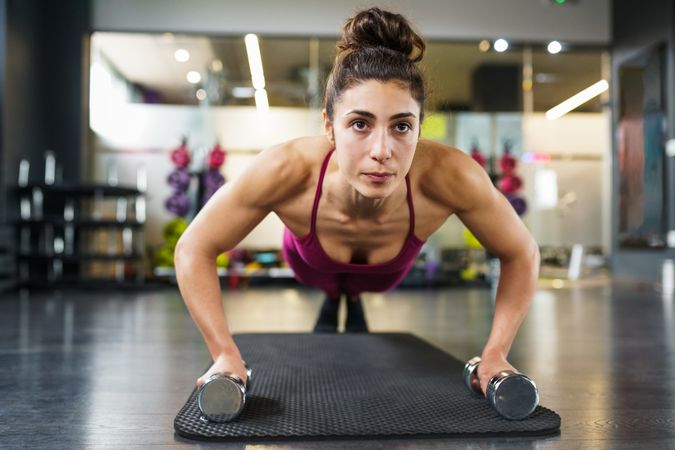 Muscular woman doing push ups while holding weights