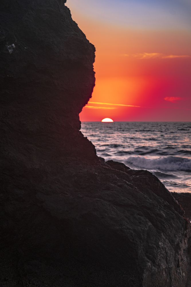 Colorful dusk seen from behind cliffs of rocky beach, beautiful