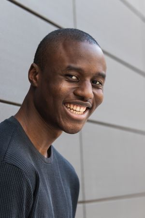 Happy young Black male standing near wall