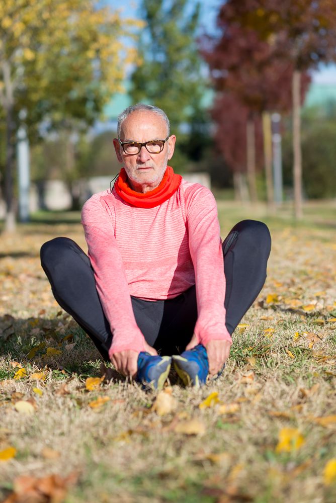 Male sitting stretching legs in grass in park