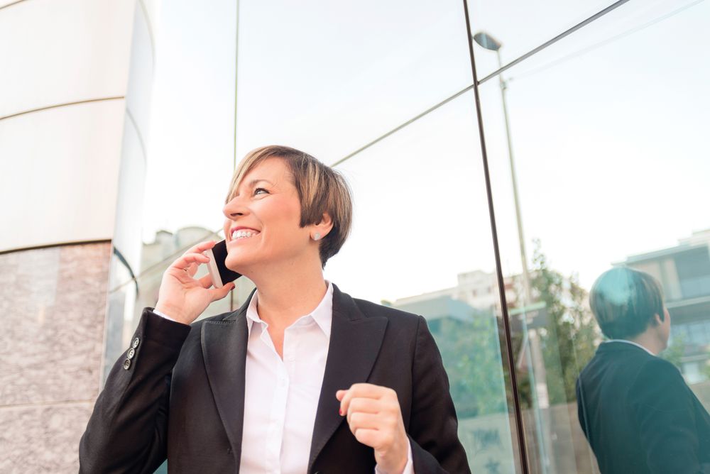 Happy businesswoman in blazer speaking on cellphone outside