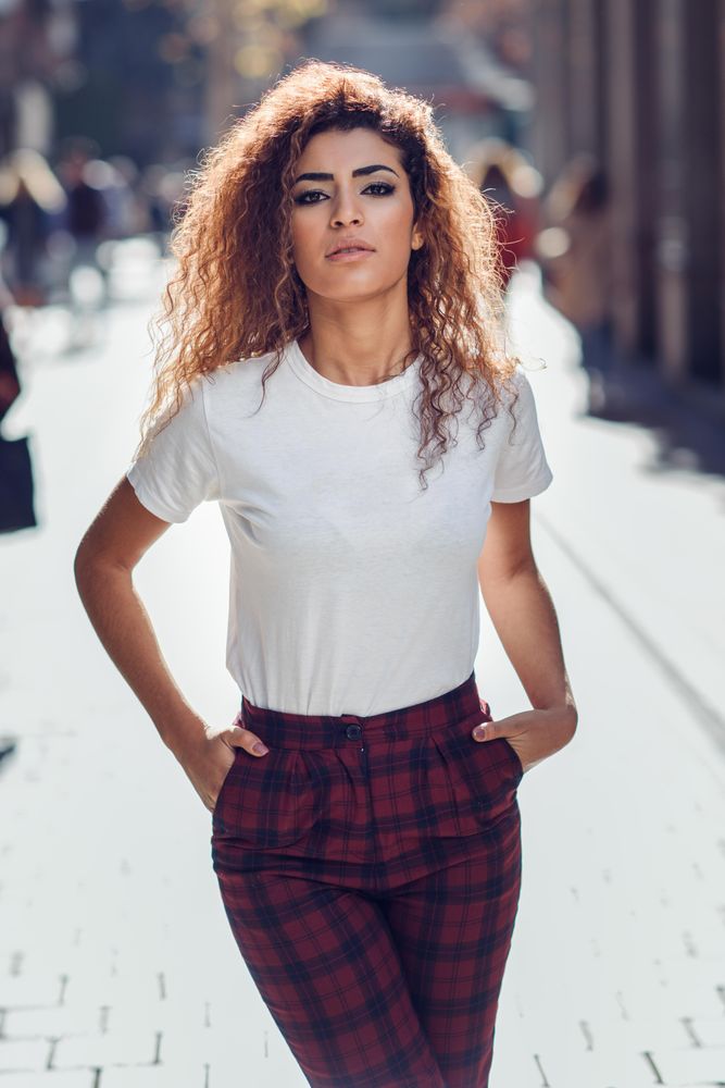 Happy Arab woman with curly hair walking down sunny street