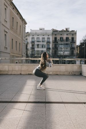 Side view of young woman doing a squat alone on a city roof top