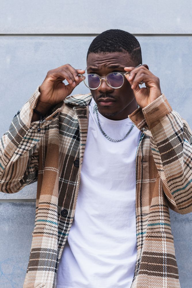 Stylish Black male standing near wall and putting on glasses