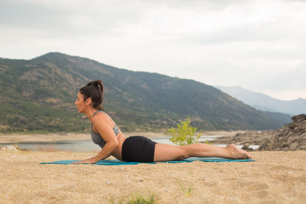 Woman practicing yoga outdoors near water