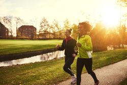 Two women jogging in windbreakers in a sunny park