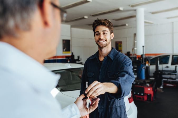 Mechanic giving car key to customer after servicing at garage
