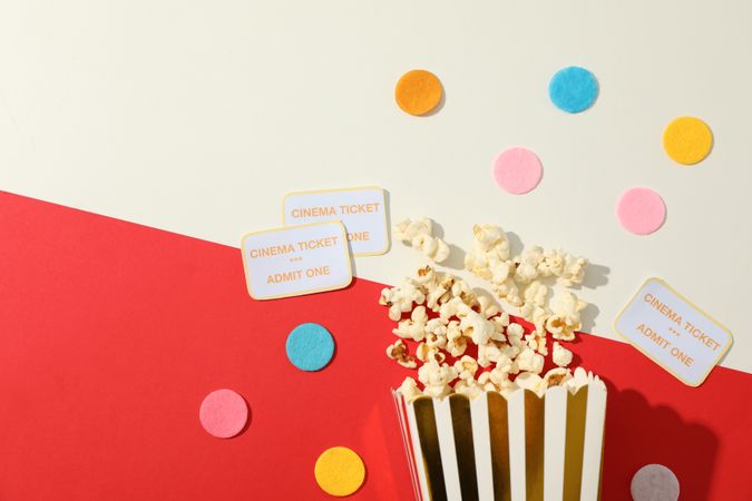 Flat lay. Confetti, tickets and box with popcorn on two tone background