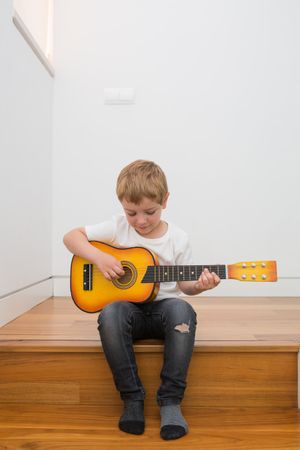 Young blonde boy playing toy guitar
