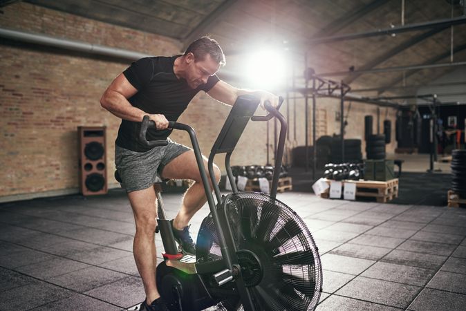 Athletic male using exercise bike in brick gym warehouse