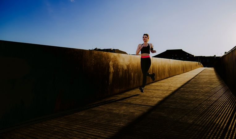 Woman running on walkway in sunny day with blue sky