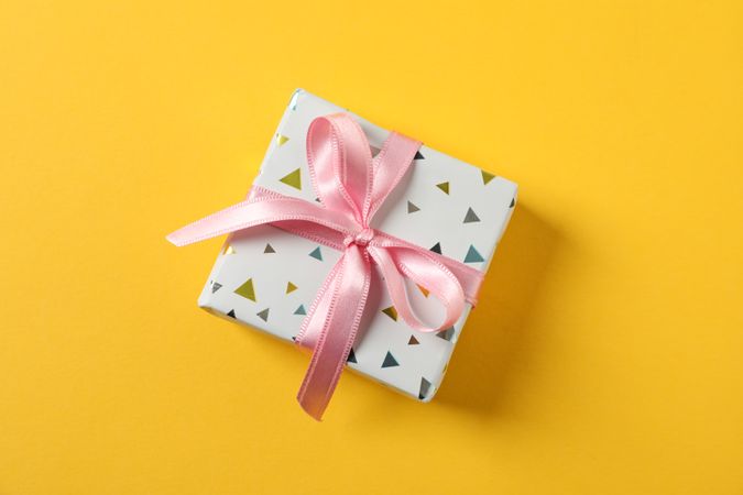 Gift box with bow on yellow background, space for text