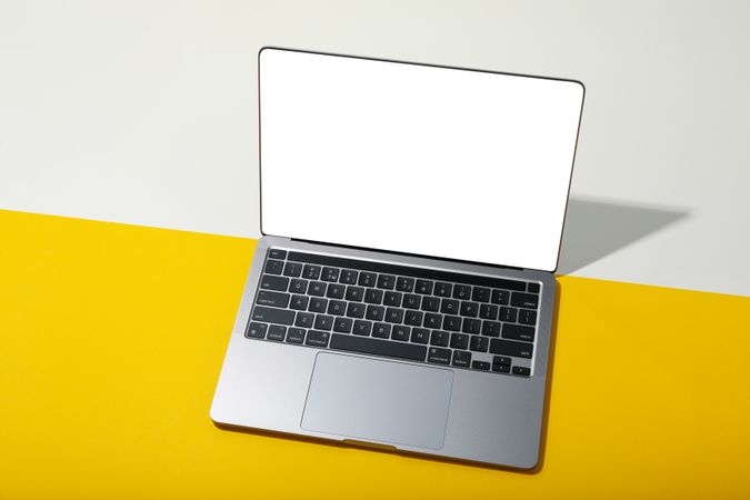 Laptop with mockup screen on yellow table leaning against wall