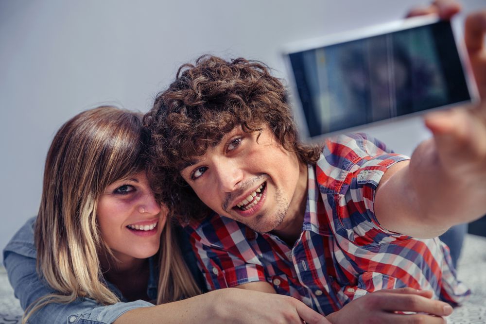 Cute couple taking selfie with smartphone on bed