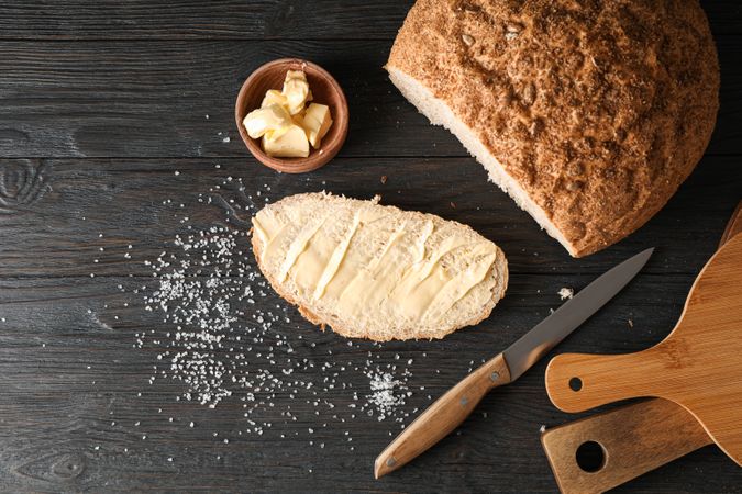Cutting boards, bread, salt, knife and butter on wooden background, top view and space for text