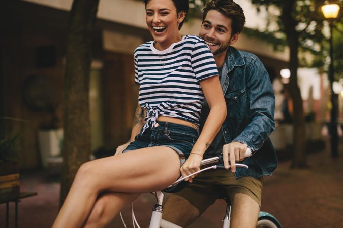 Man riding bicycle with his girlfriend sitting on handlebar