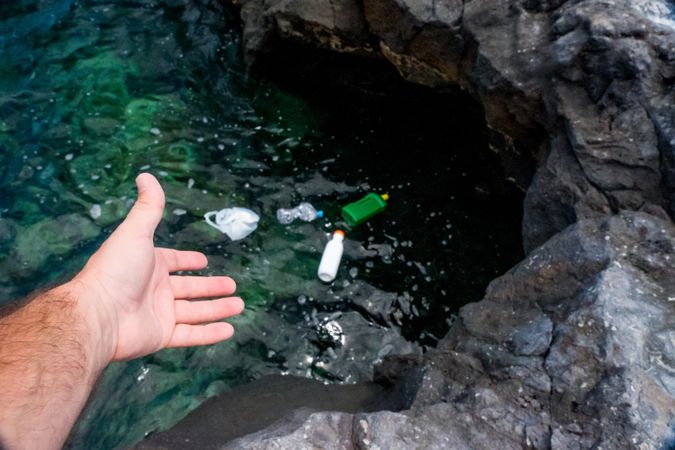 Crop man pulling plastic bag out of water