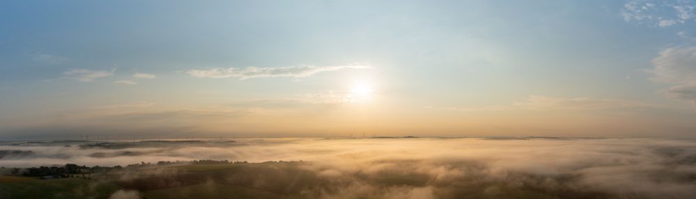 Drone panorama with golden light illuminating foggy agricultural fields and rolling hills