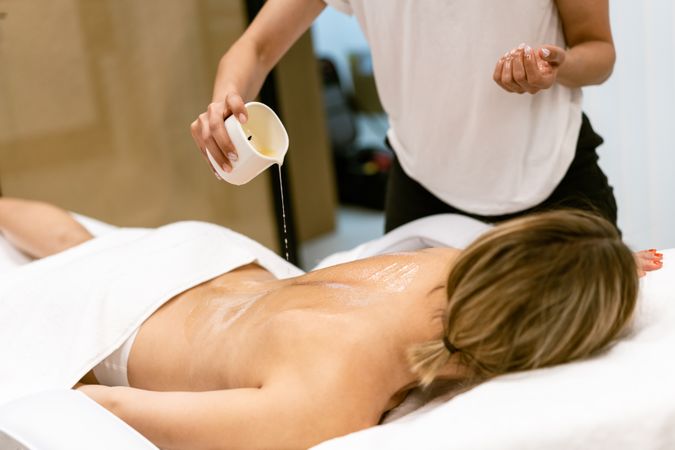 Masseuse pouring oil on back of female client