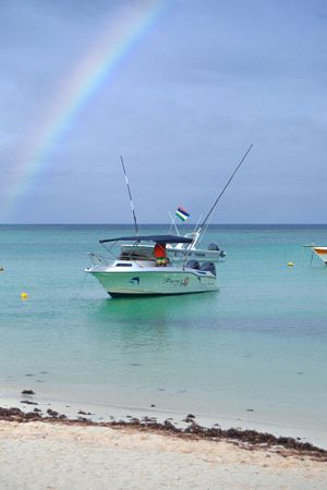 Man on boat near beach under rainbow