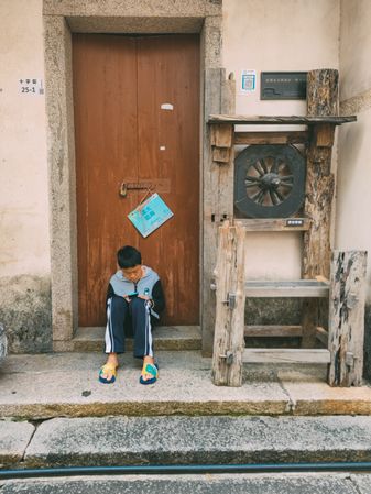 Boy sitting on doorstep using smartphone in Dapeng, Shenzhen, China