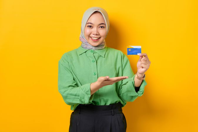 Smiling Muslim woman in headscarf and green blouse presenting her credit card