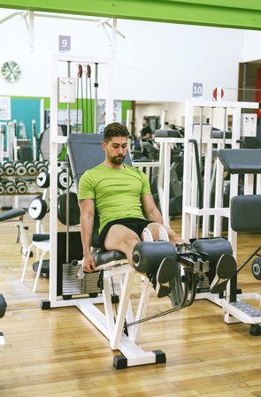 Male in green t-shirt working out quads on leg machine