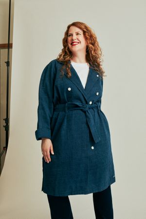 Woman in long blue coat standing in front of studio backdrop