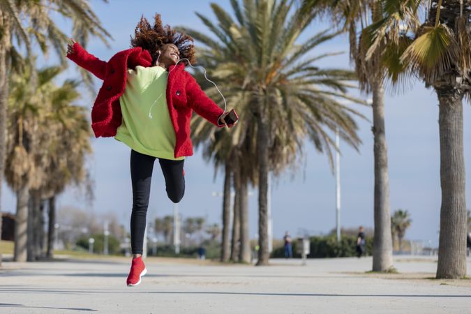 Female jumping while listening to music outside on street with palm trees