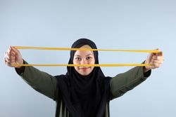 Young Asian Hijab Woman Stretch Yellow Resistance Band for Hand Pilates Exercise