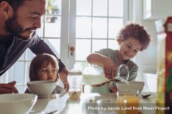 Man watching his child pour milk in his breakfast bowl bG3Nxb
