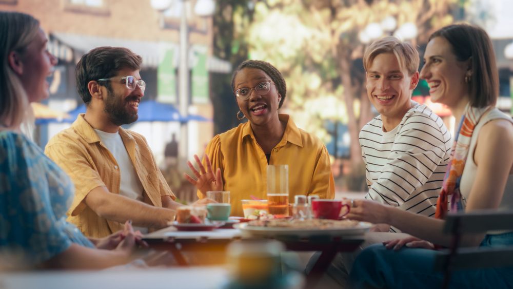 Men and Women Sitting Behind a Table, Socializing on a Summer Terrace of a Street Cafe