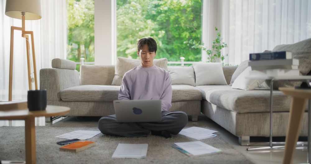 Young Asian Male Browsing Internet, Using Laptop Computer at Home.