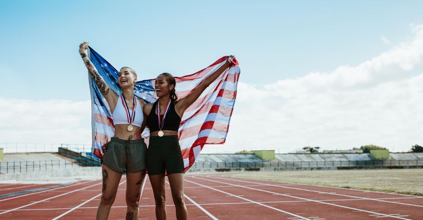 Two female athletes celebrating victory holding American flag on running track