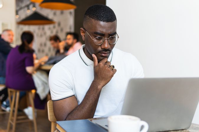 Serious Black man using laptop at table in cafe