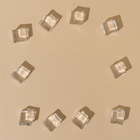 Flat lay of ice cubes on border of beige background with shadows