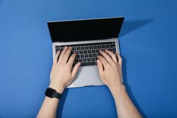 Looking down at person on laptop with blank screen in blue room