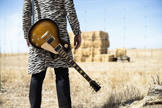 Person with guitar behind back in front of barbed wire