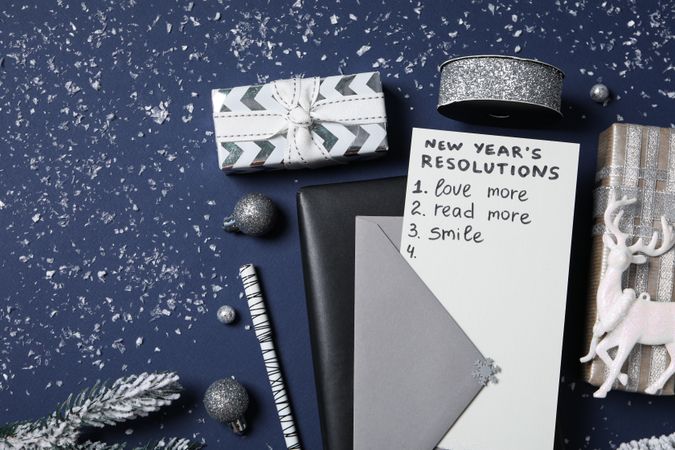 Paper with list, gift boxes and decorations on blue background, top view